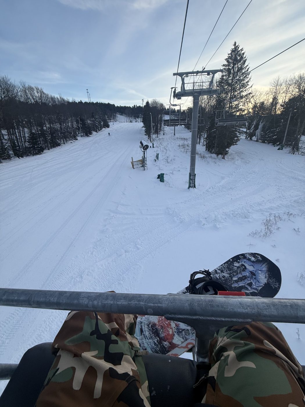 View from a chairlift over a snowy trail, snowboard resting on the bar
