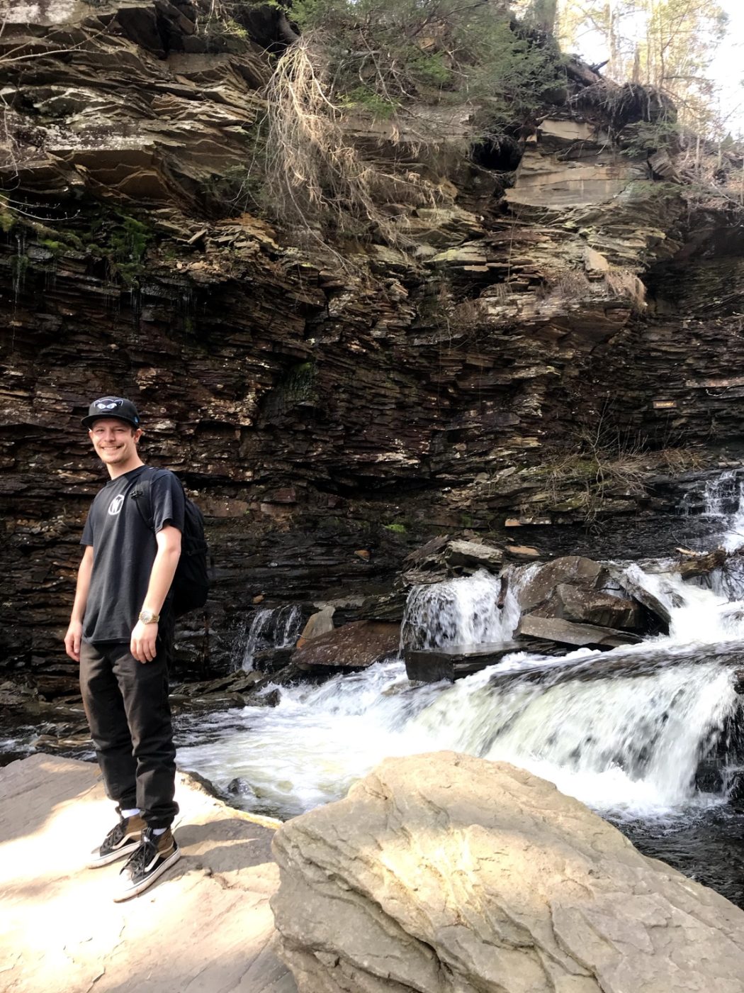 Alex standing on a rock beside a waterfall on a hiking trail